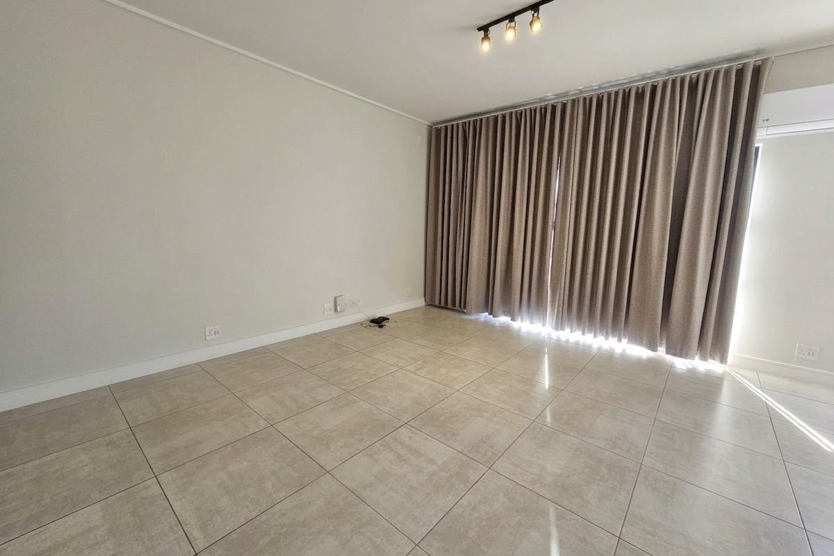 A bright, empty living room featuring neutral tiled flooring, modern track lighting, and floor-to-ceiling curtains covering a large window or sliding door.