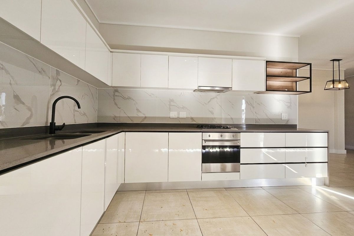 Modern kitchen featuring high-gloss white cabinetry, stone countertops, marble-look splashback, and integrated stainless steel appliances in a clean, open-plan layout.