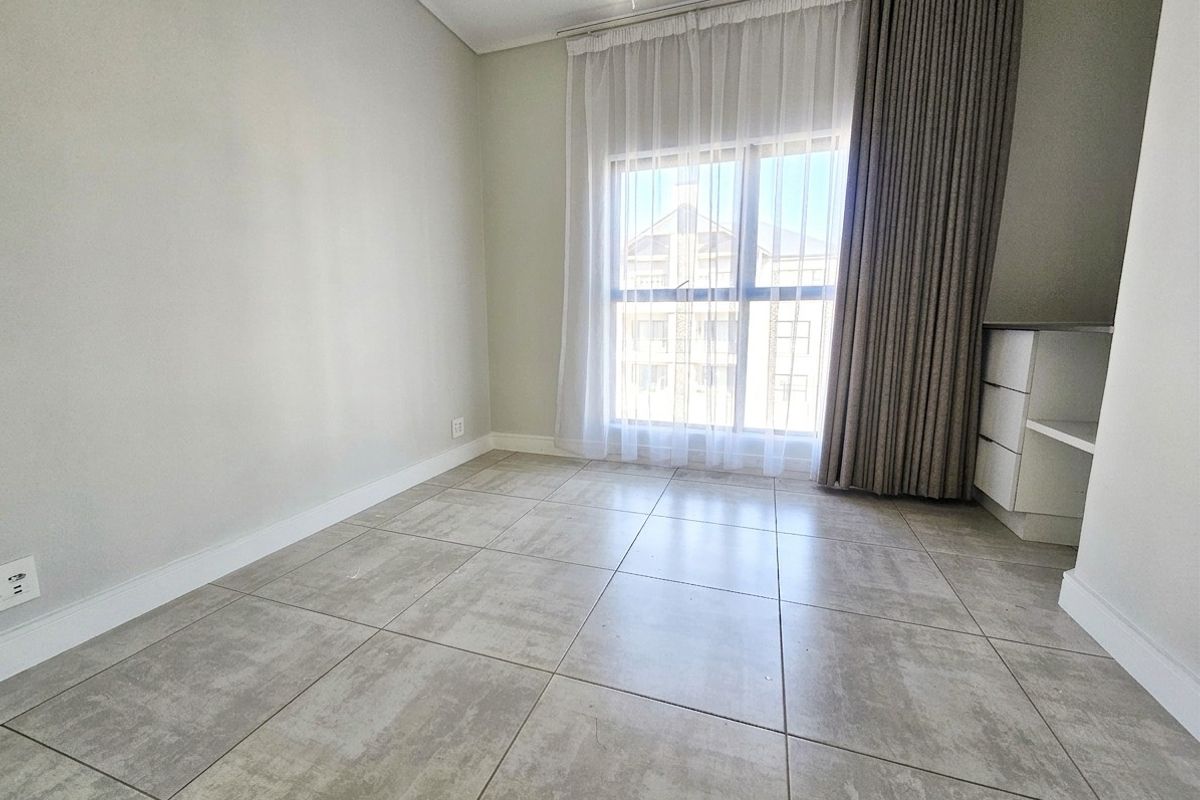 A bright, empty bedroom featuring neutral tiled flooring, built-in cabinetry, and large windows with installed curtain tracks.