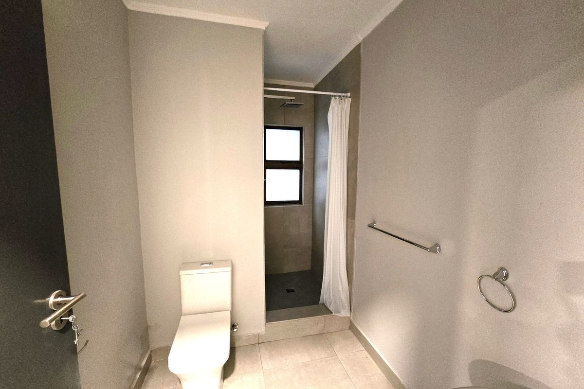 A clean, functional bathroom featuring a walk-in shower, modern toilet, and neutral tiled finishes.