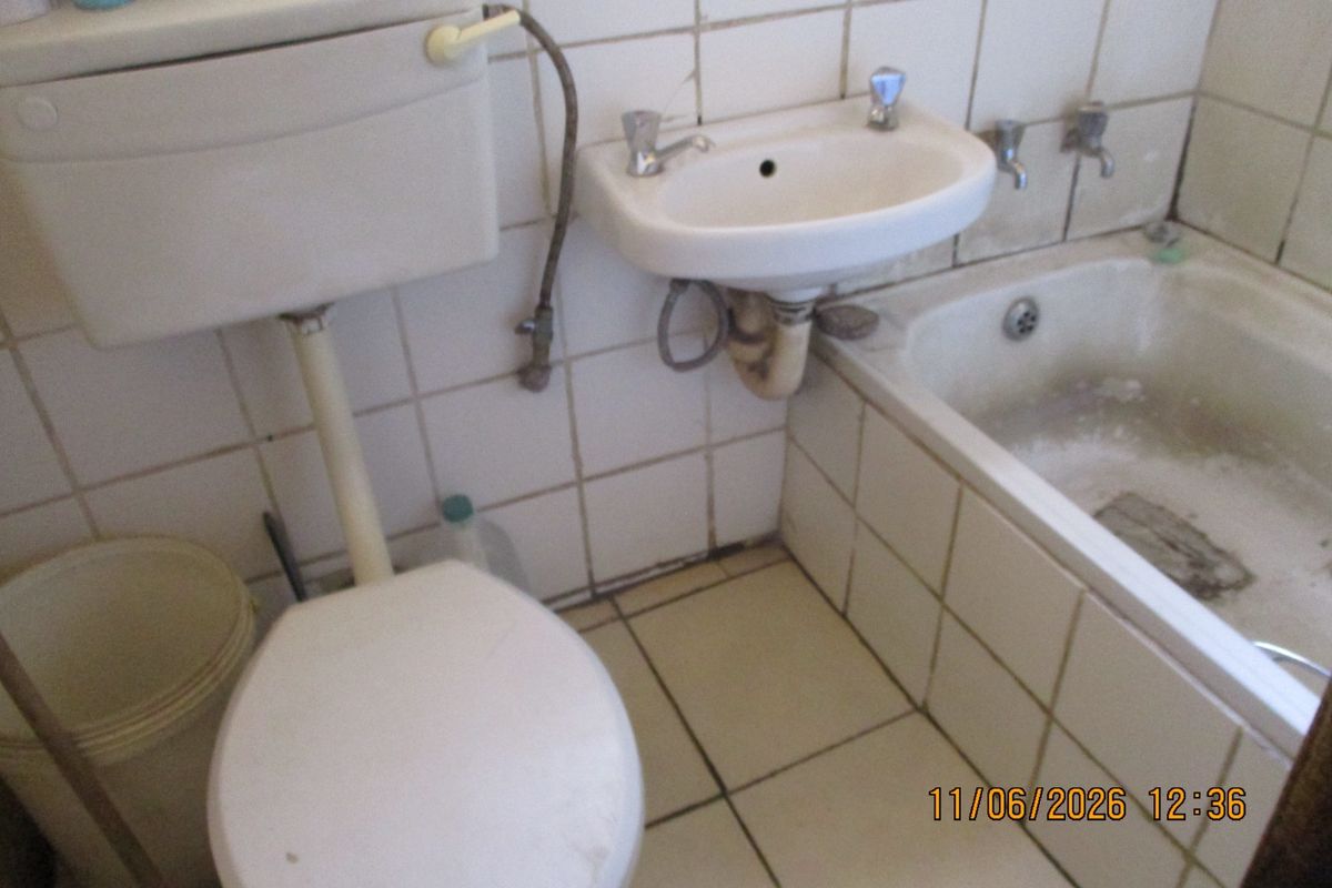 A dated bathroom featuring a standard bathtub, wall-mounted basin, and toilet with white tiled walls and flooring.