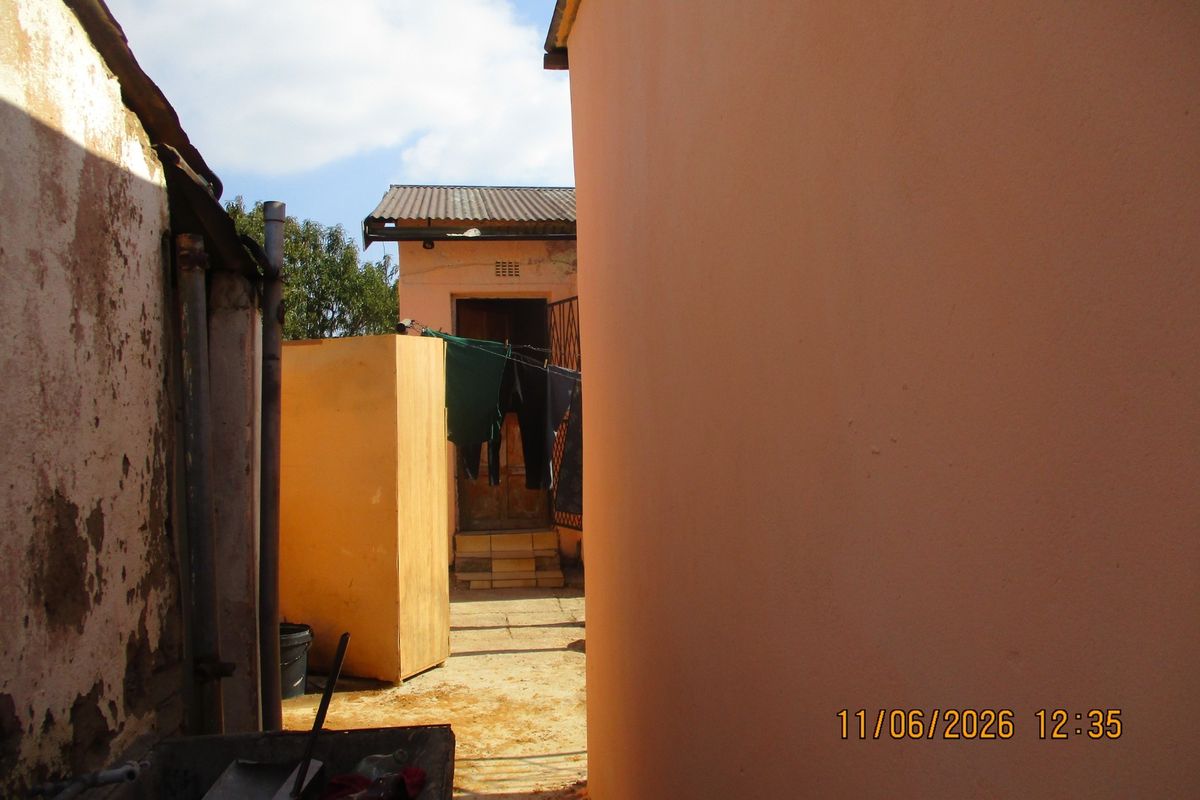 A narrow exterior passage between building structures showing weathered walls and basic utility access.