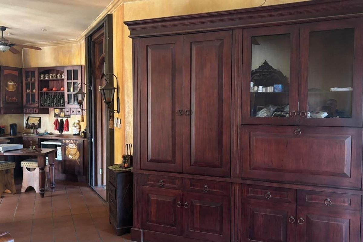 A rustic-style kitchen area featuring dark wood cabinetry, terracotta floor tiles, and a ceiling fan, creating a warm and traditional atmosphere.