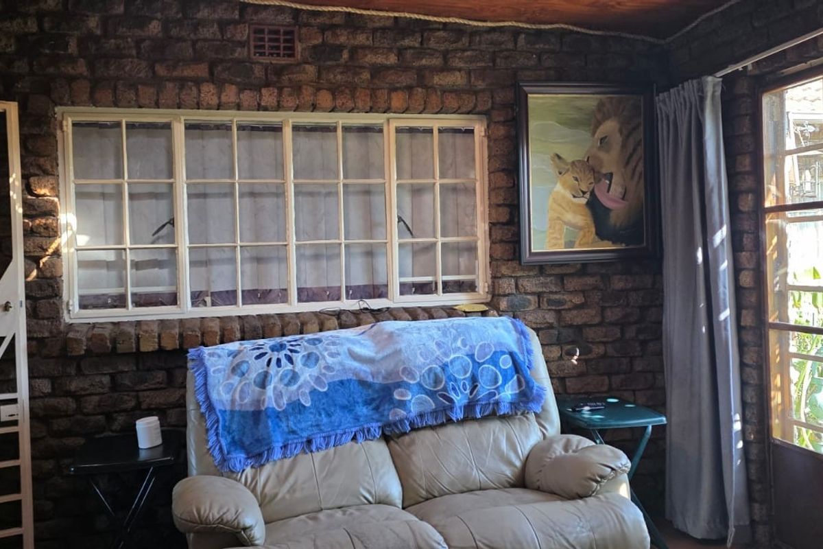 A rustic living area featuring exposed face-brick walls, large multi-pane windows, and a secure metal security gate.