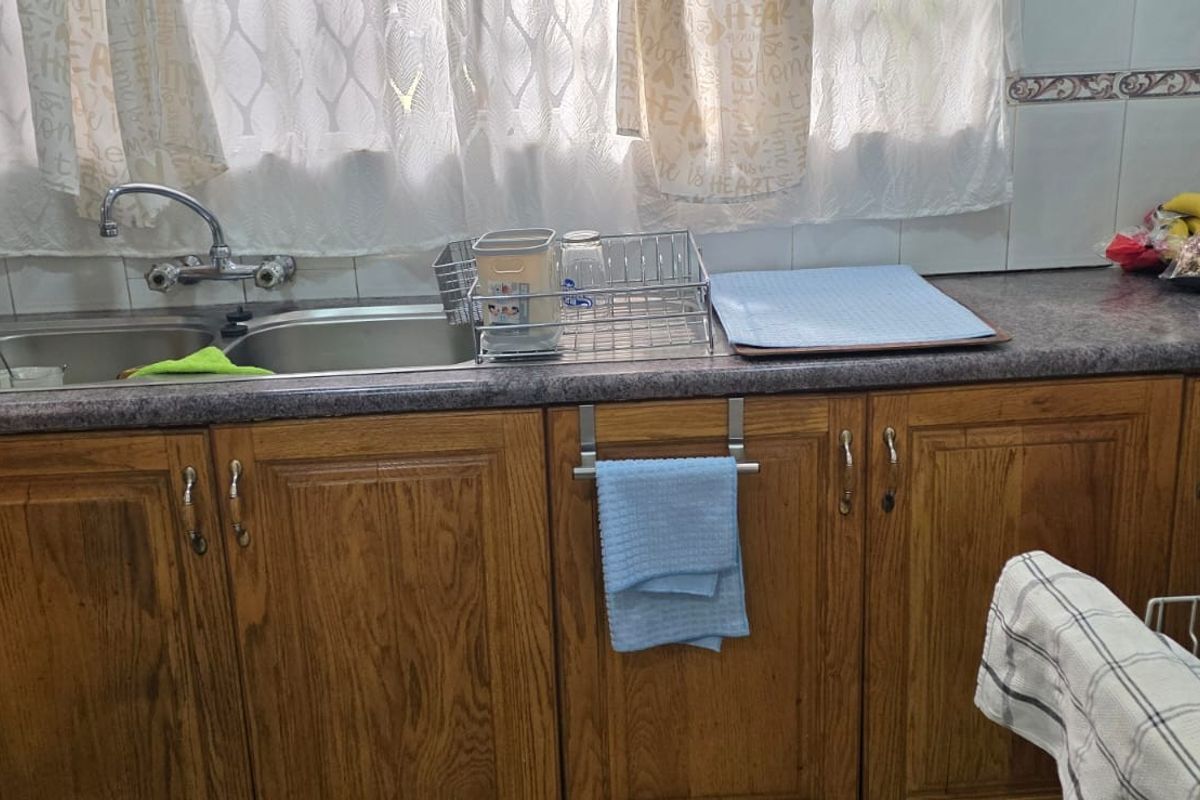 A functional kitchen area featuring wooden cabinetry, a double stainless steel sink, and tiled splashbacks.