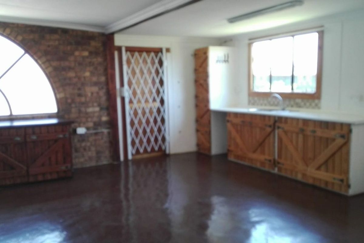 A rustic kitchen area featuring exposed brickwork, a distinctive arched window, wooden cabinetry, and a security gate.