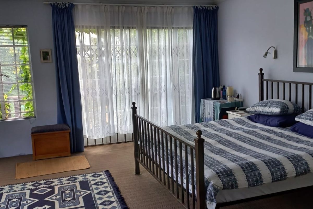 A spacious bedroom featuring large windows, sliding glass doors with security gates, and wall-mounted reading lights.
