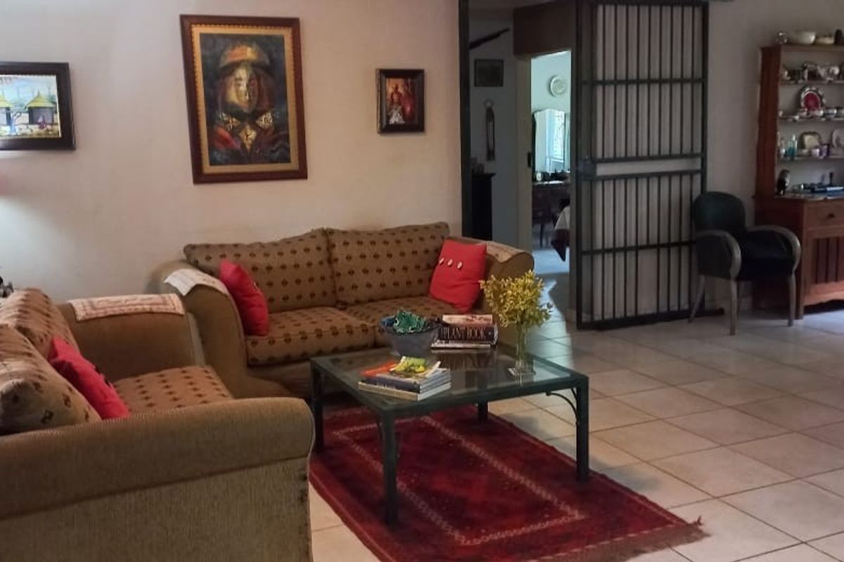 A spacious living room featuring tiled flooring and a secure metal gate leading to the bedroom area.