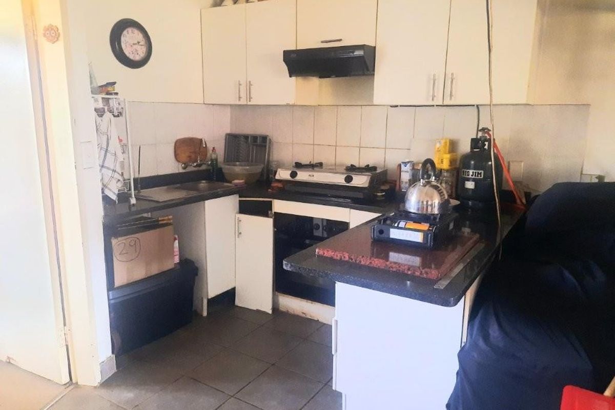 Compact kitchen featuring white cabinetry, tiled backsplash, and a built-in oven with hob, requiring cosmetic updates to modernize the space.