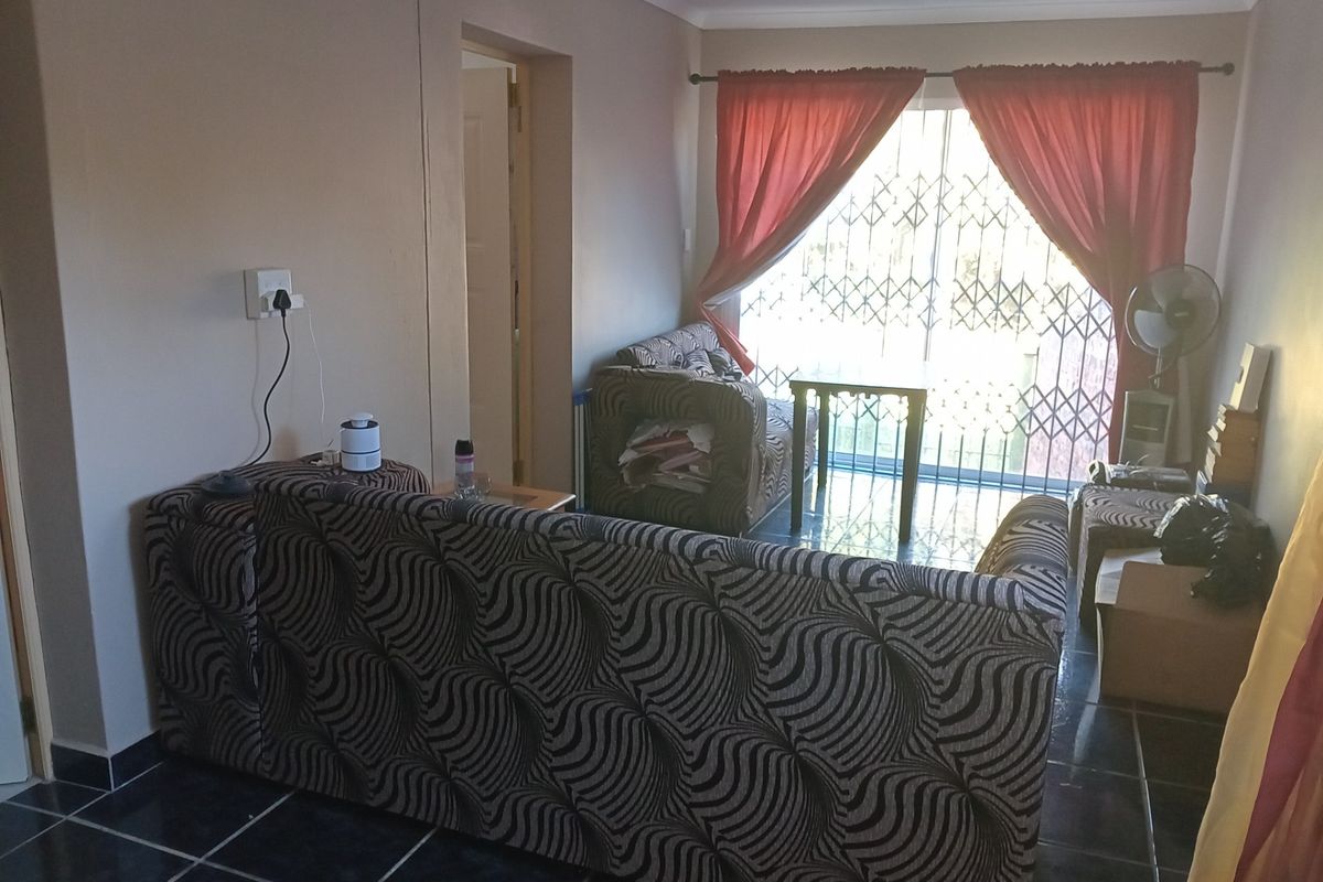 A living room featuring dark tiled flooring, a sliding glass door with security gate, and access to an adjacent room.