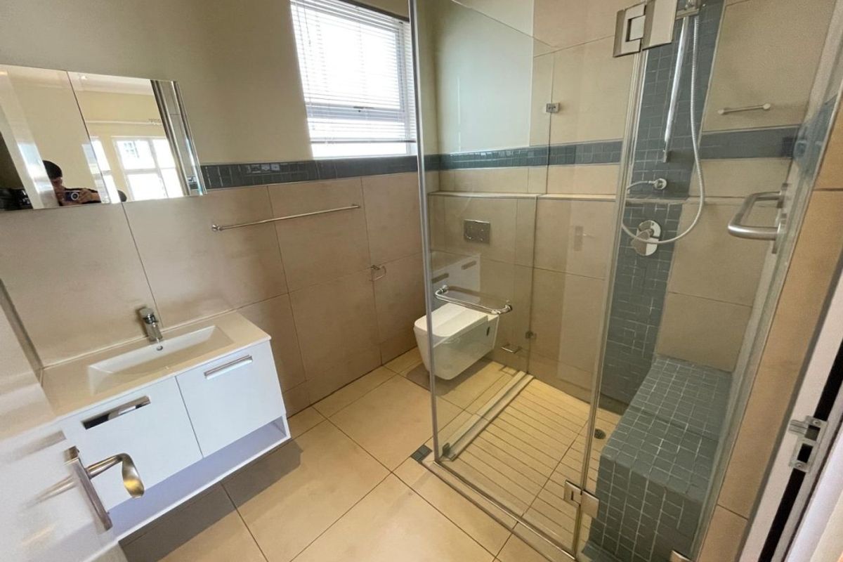 Modern bathroom featuring a glass-enclosed walk-in shower with built-in bench, wall-mounted toilet, and a sleek vanity unit with integrated basin.