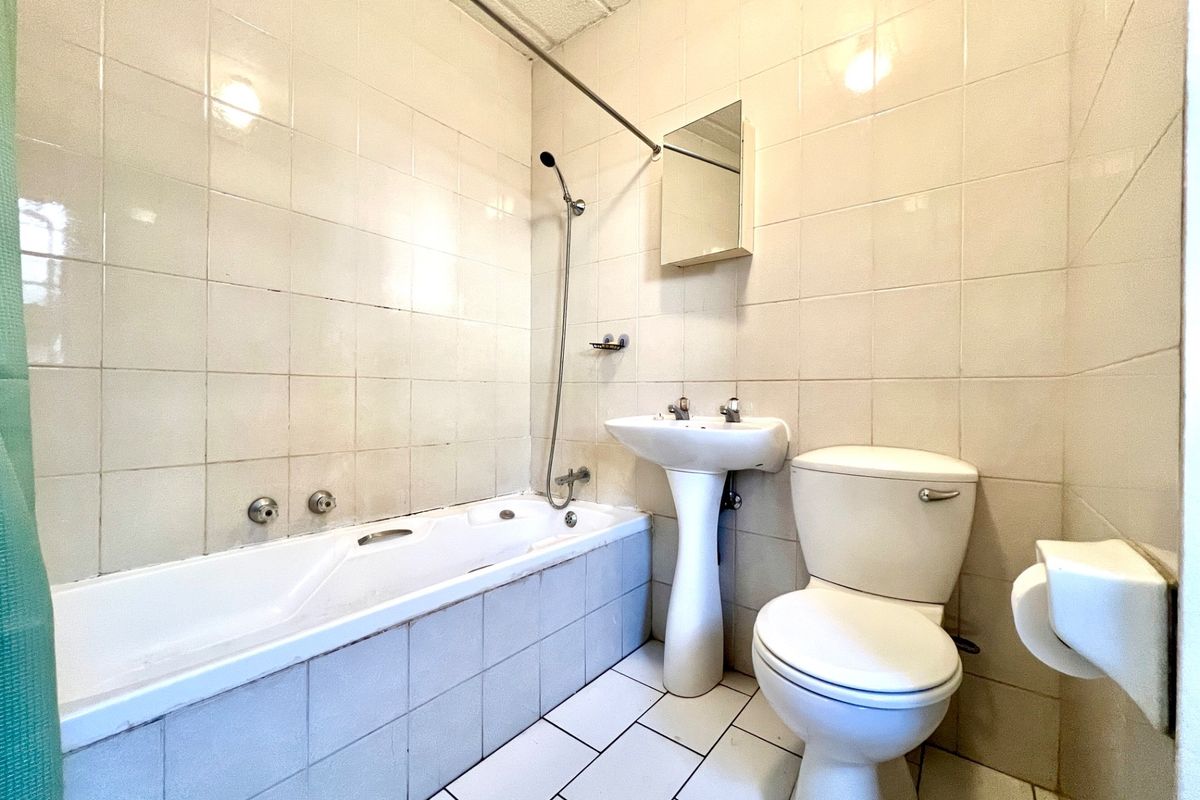 A functional bathroom featuring a bathtub with shower attachment, pedestal basin, and toilet, finished with full-height wall tiling.