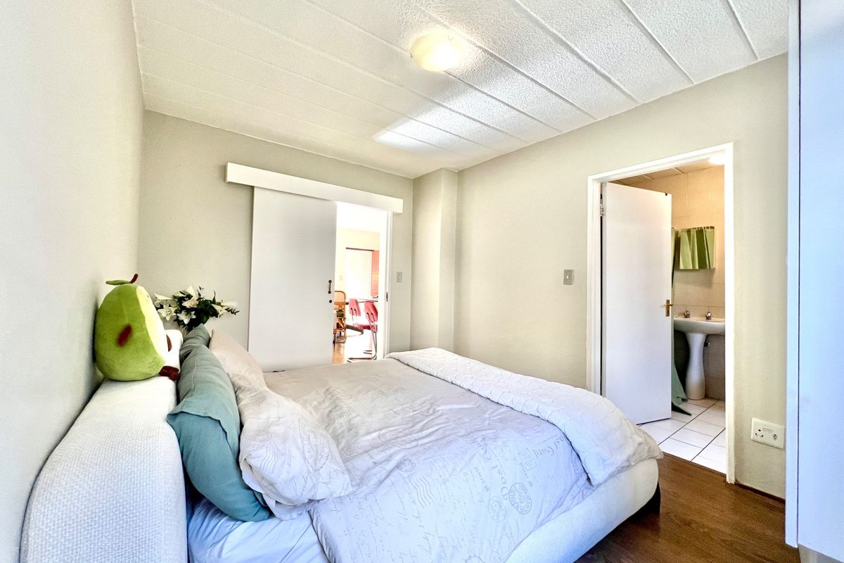 A bedroom featuring wood-look flooring, a textured ceiling, and an en-suite bathroom with a pedestal basin.