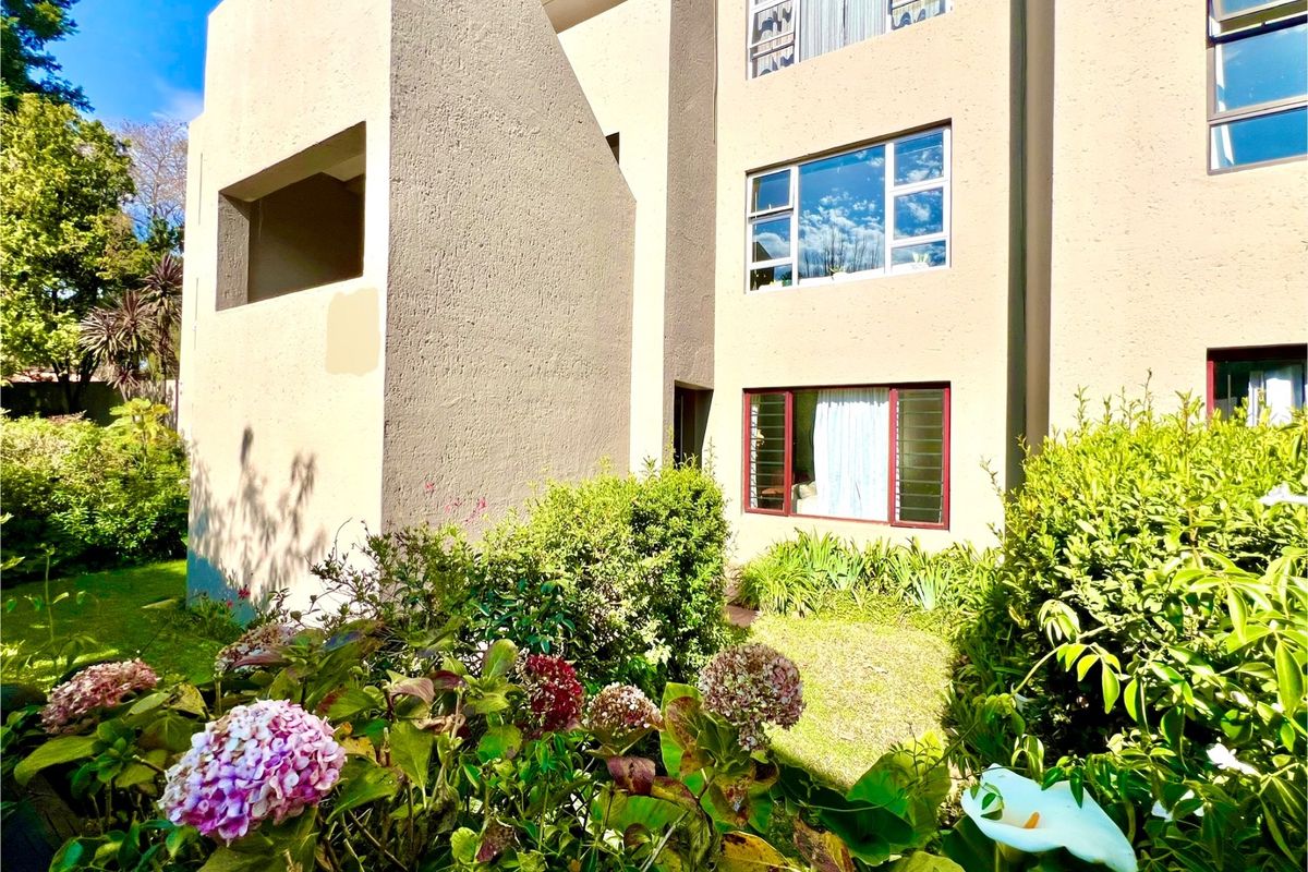 A view of the apartment building exterior featuring a landscaped garden, mature shrubs, and multi-level windows with security bars.