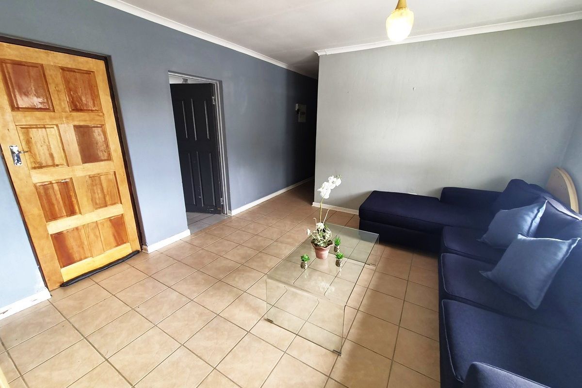 A living room featuring tiled flooring, a solid wood entrance door, and a neutral grey wall finish.