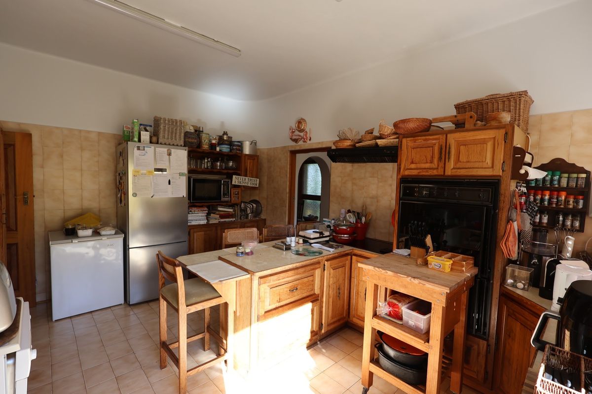 A functional kitchen featuring timber cabinetry, built-in oven, tiled flooring, and a central island workspace with integrated storage.