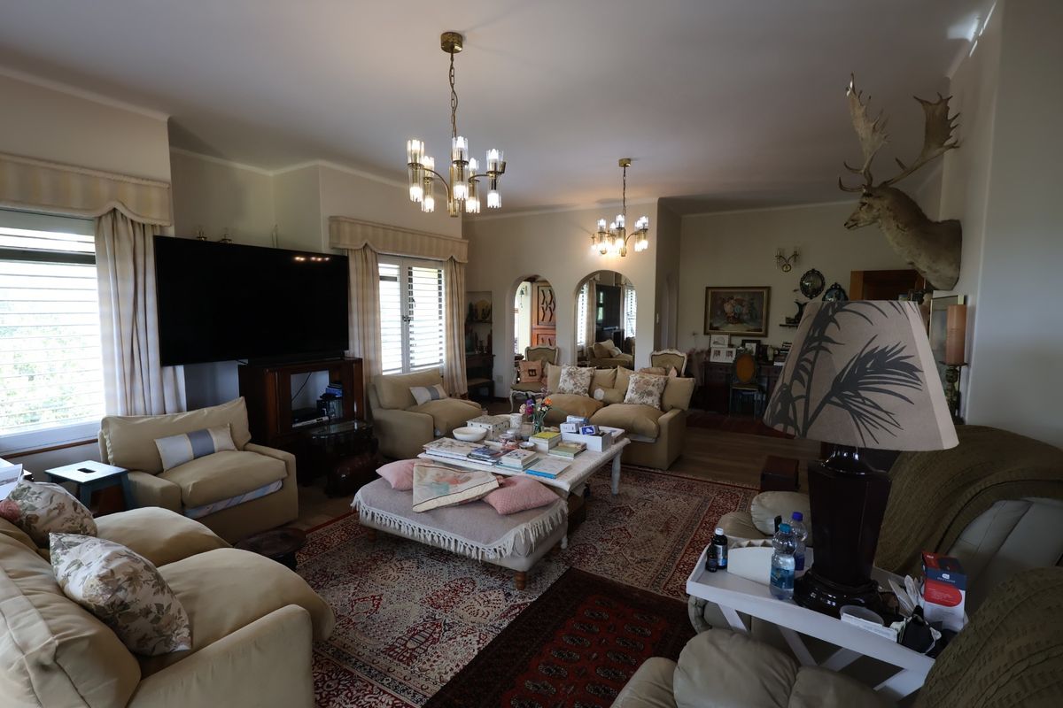Spacious living room featuring dual chandeliers, arched doorways, and large windows with integrated shutters, providing a comfortable and traditional living space.
