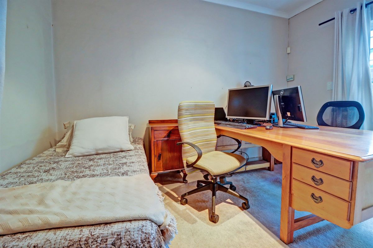 A functional bedroom currently utilized as a home office, featuring neutral wall finishes and carpeted flooring.