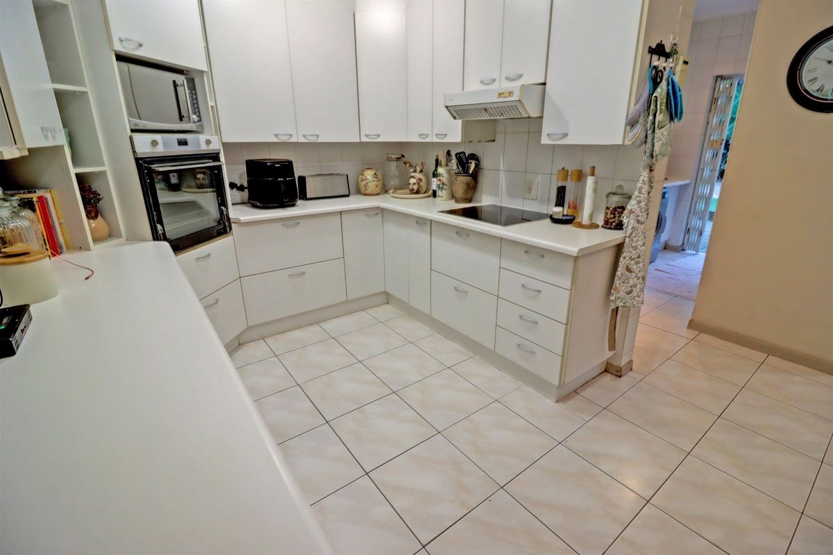 A functional kitchen featuring white cabinetry, built-in oven and microwave, electric hob with extractor fan, and tiled flooring.