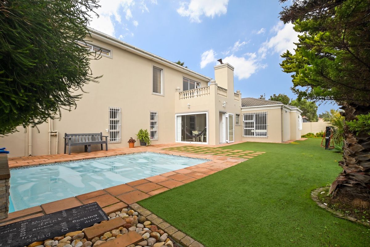 Rear view of the property featuring a swimming pool, paved patio area, and a well-maintained lawn with established garden surroundings.