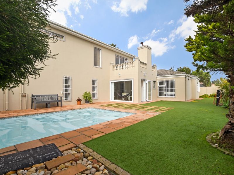 Rear view of the property featuring a swimming pool, paved patio area, and a well-maintained lawn with established garden surroundings.