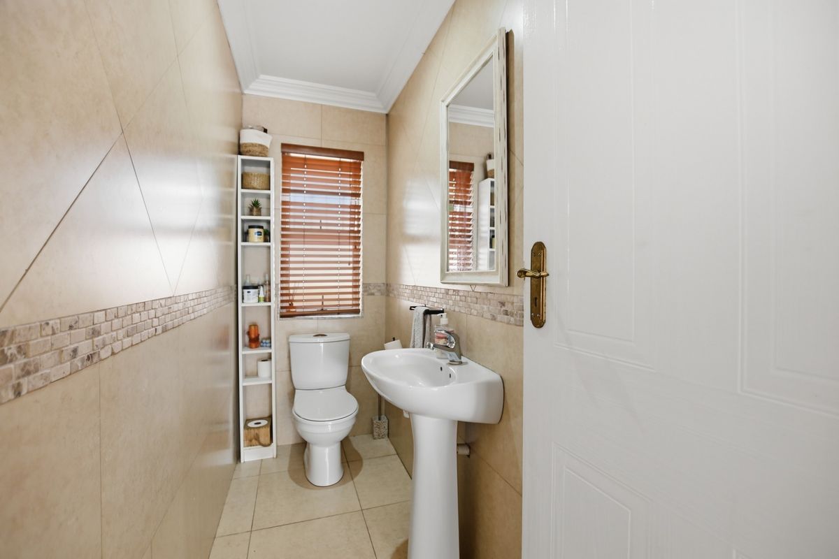 A compact guest bathroom featuring a pedestal sink, a modern toilet, and neutral wall tiling with a decorative mosaic border.