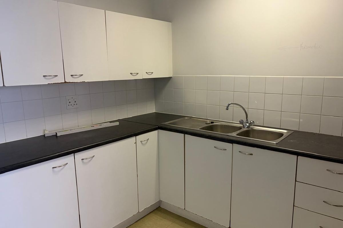 A functional kitchenette area featuring white cabinetry, dark laminate countertops, a double stainless steel sink, and tiled splashbacks.