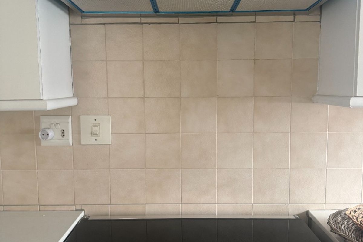 A kitchen cooking area featuring a stainless steel extractor fan, tiled backsplash, and a built-in electric stove with a glass cooktop.