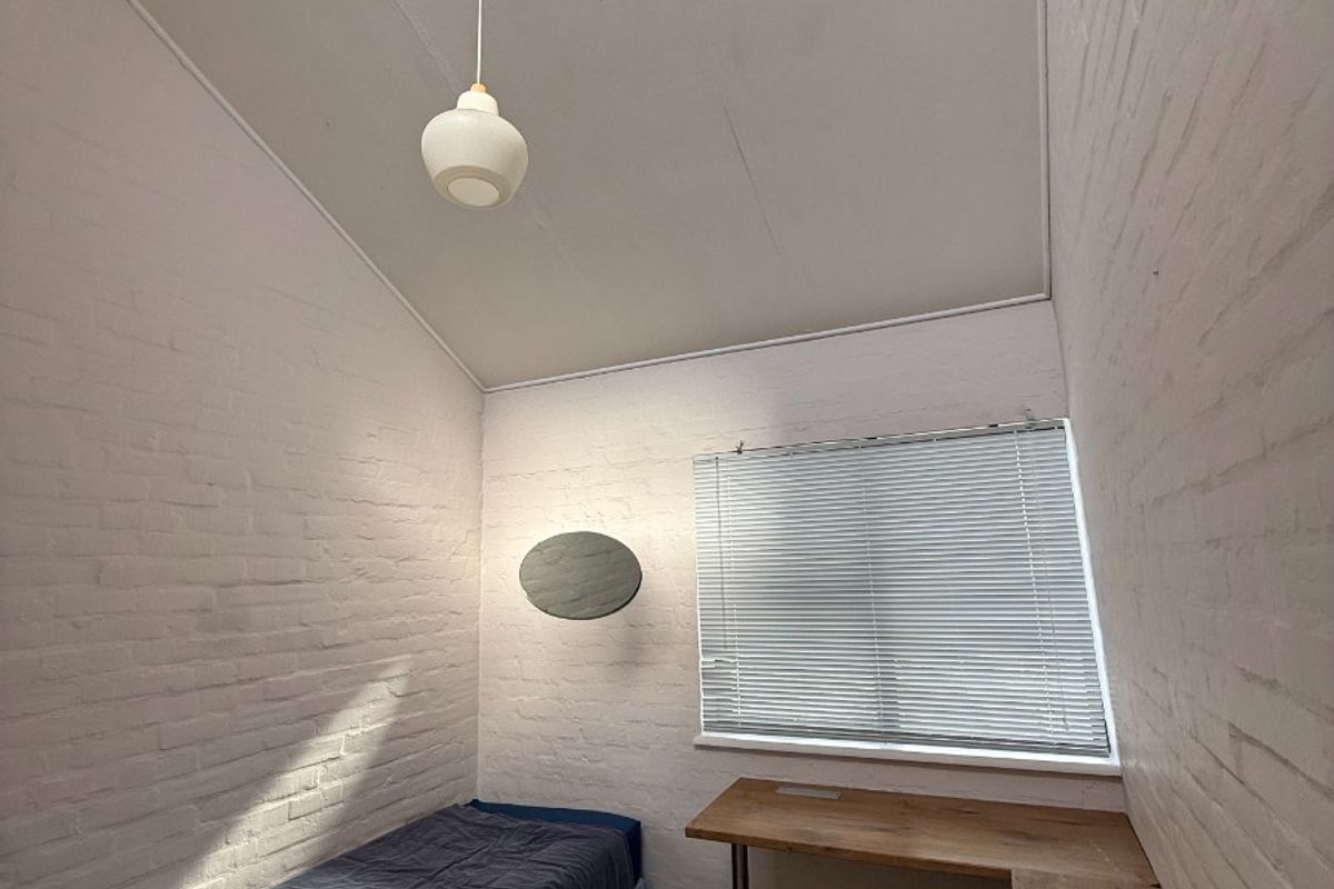 A compact bedroom featuring painted brick walls, a built-in wooden desk, and a single pendant light fixture.