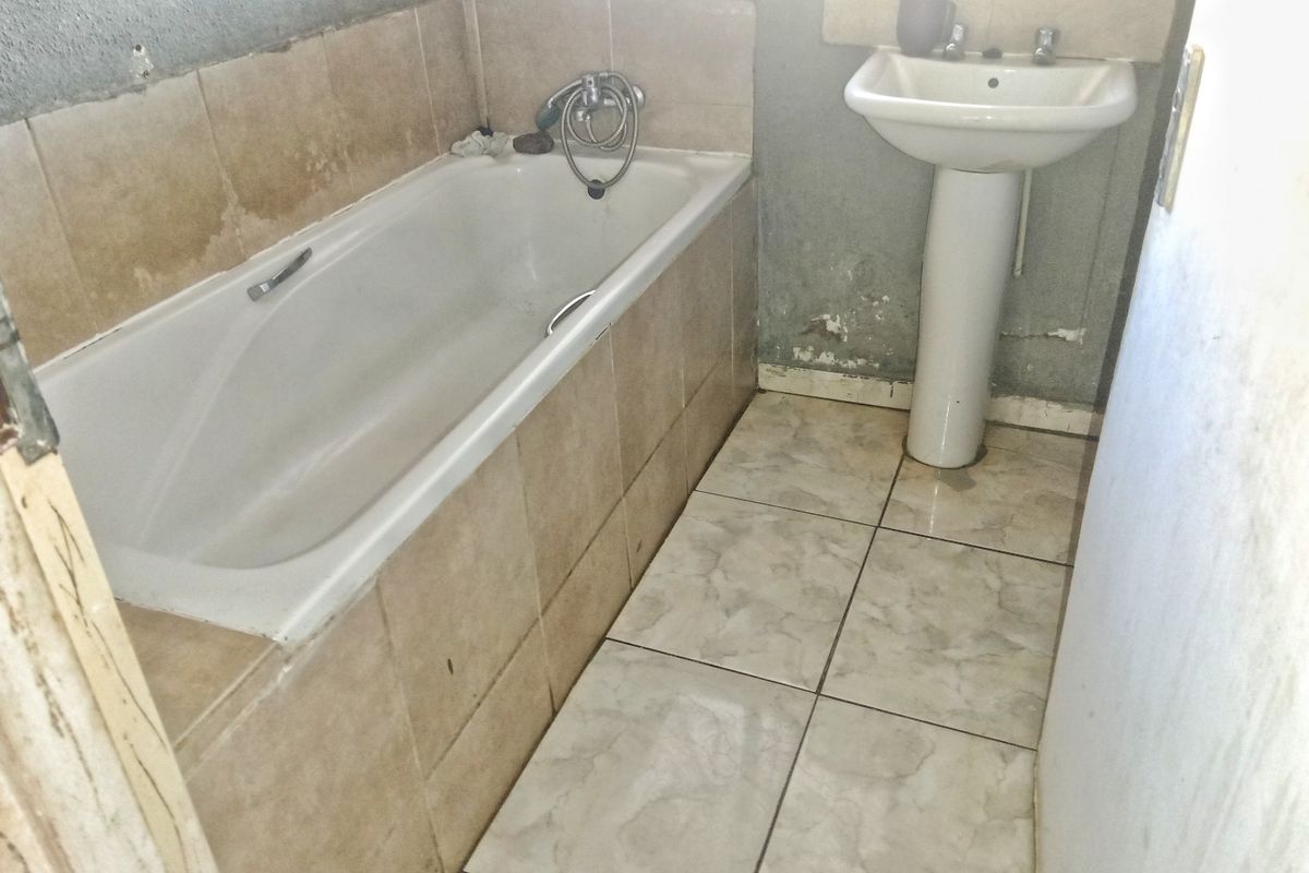 A dated bathroom featuring a built-in bathtub with tiled surround and a pedestal basin, requiring cosmetic updates and wall repairs.