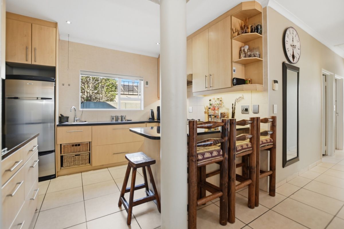 A functional kitchen featuring light wood cabinetry, dark countertops, tiled flooring, and a central structural pillar with an integrated breakfast bar.