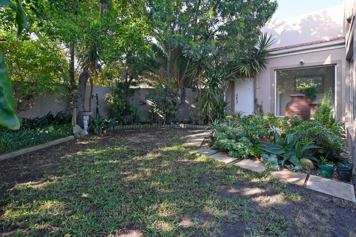 A private rear garden featuring established trees, landscaped garden beds, stone paving, and direct access to the home's exterior.