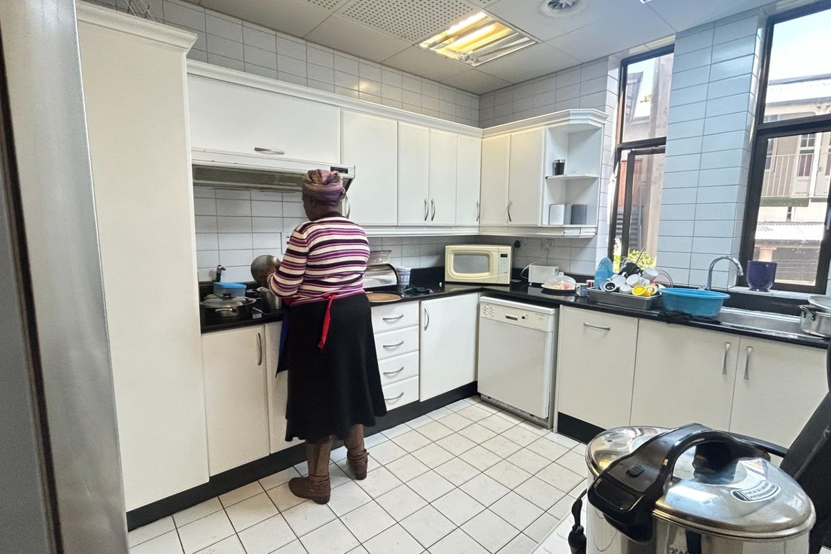 A functional commercial kitchen featuring white cabinetry, black countertops, tiled walls, and integrated appliances, providing a practical workspace for daily operations.