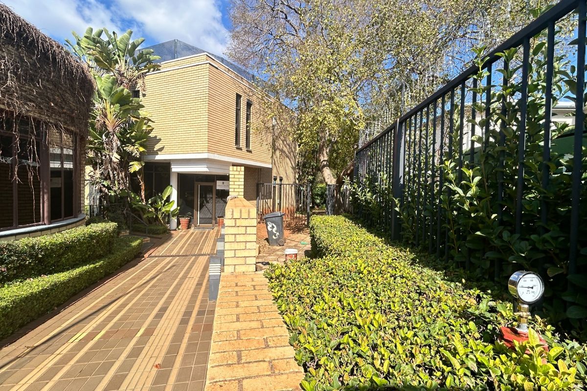 Exterior view of a commercial property entrance featuring a paved walkway, landscaped hedges, and secure perimeter fencing.