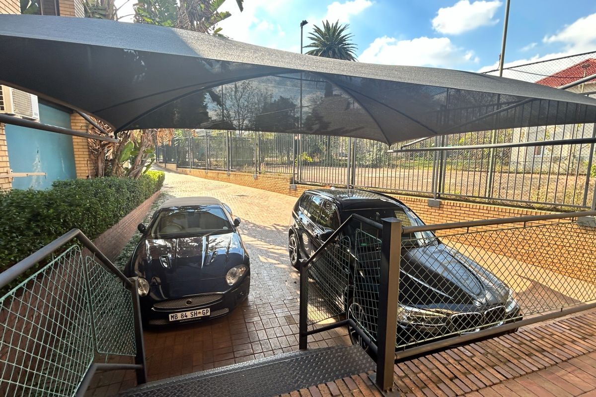 Outdoor parking area featuring paved driveway, shade sail structure, and perimeter fencing, providing secure off-street parking for the commercial property.