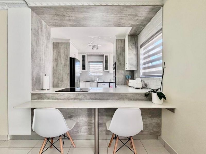 Modern kitchen featuring a breakfast bar, stone-look cabinetry, integrated cooktop, and tiled flooring, offering a functional and stylish culinary space.