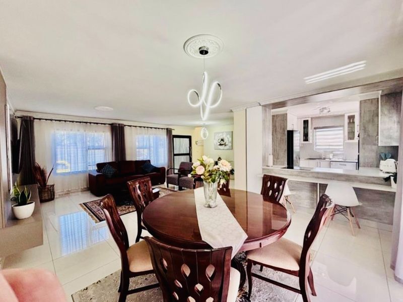 An open-plan living and dining area featuring polished floor tiles, a modern ceiling light fixture, and a breakfast bar overlooking the kitchen.