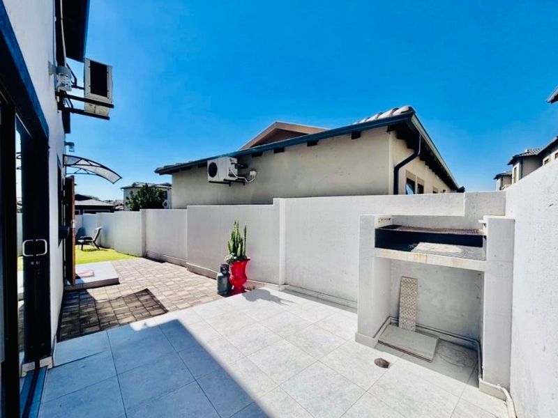 A private rear patio area featuring a built-in braai, paved flooring, and perimeter walling, providing a functional outdoor entertainment space.