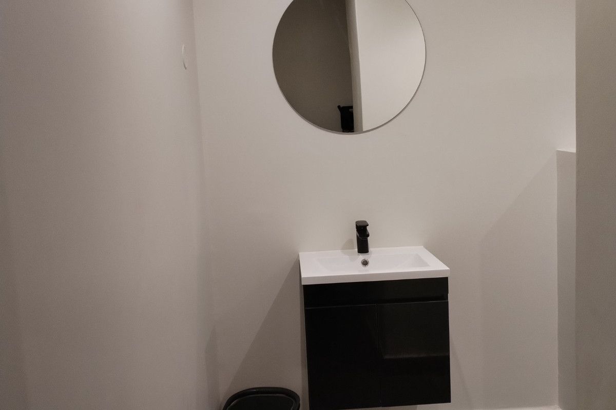 A minimalist guest bathroom featuring a modern wall-mounted vanity with a black mixer tap and a circular mirror.