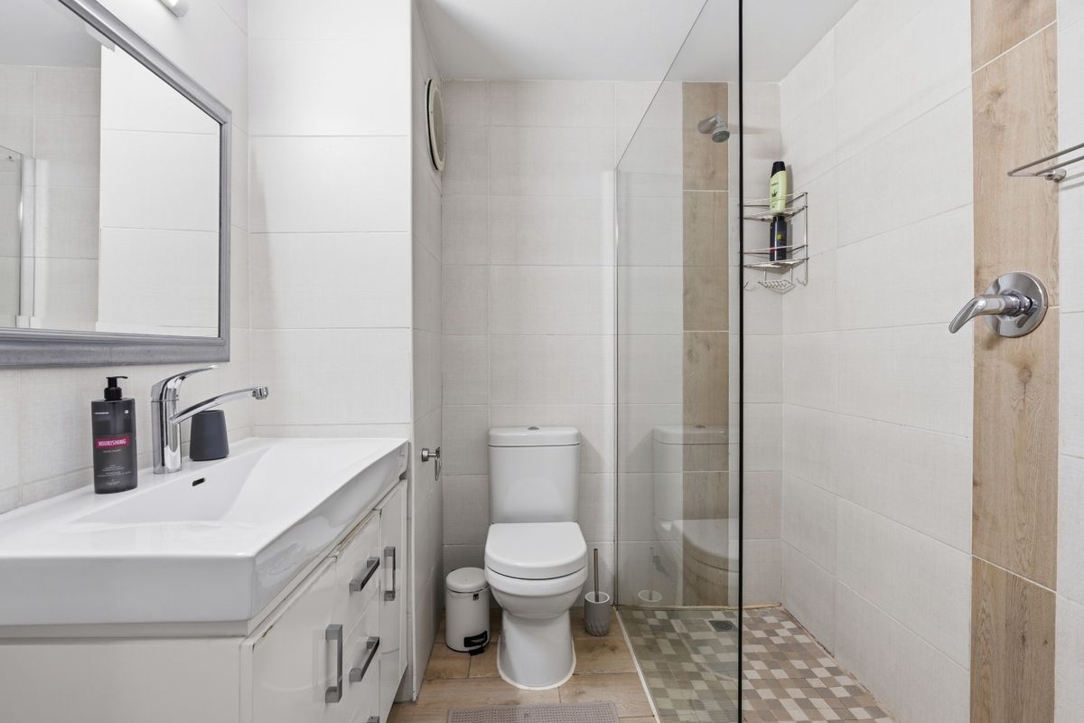 Modern bathroom featuring a glass-enclosed walk-in shower, wall-mounted vanity with basin, and a white toilet with neutral tiled finishes.