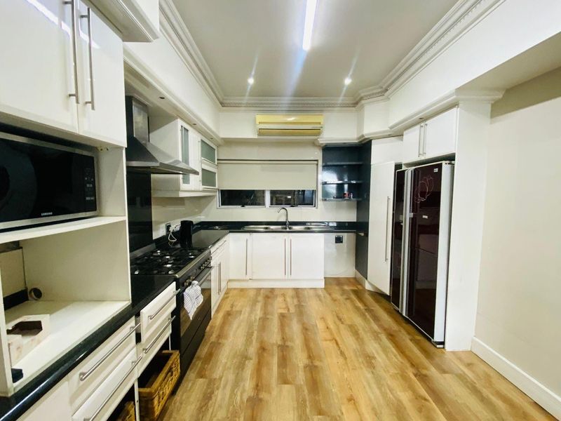 Modern kitchen featuring white cabinetry, dark granite countertops, integrated appliances, gas hob, and wood-look laminate flooring.