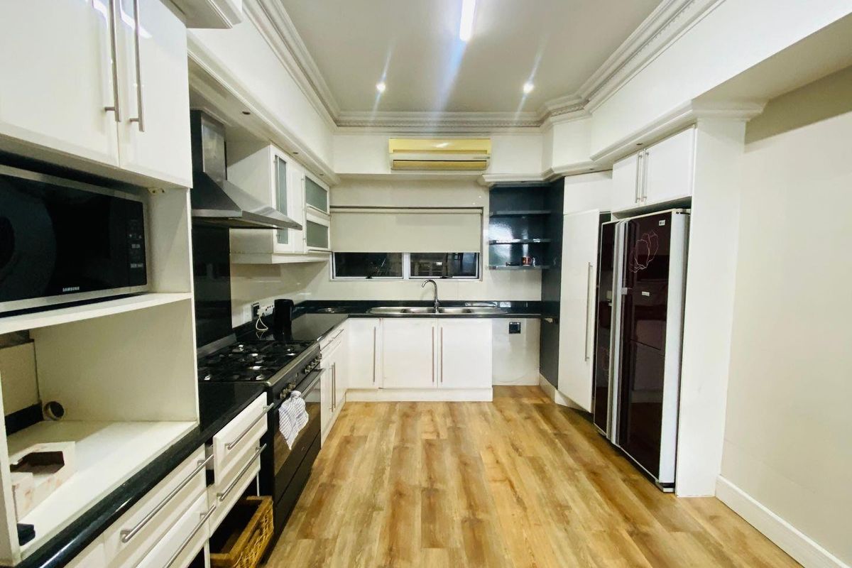 Modern kitchen featuring white cabinetry, dark granite countertops, integrated appliances, gas hob, and wood-look laminate flooring.