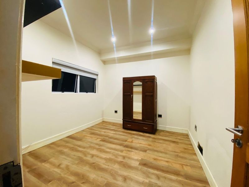 A bright, empty bedroom featuring modern laminate flooring, recessed downlighting, and a window with a fitted roller blind.