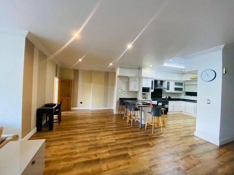 Spacious open-plan living area featuring modern kitchen cabinetry, granite countertops, breakfast bar, and warm laminate flooring throughout.