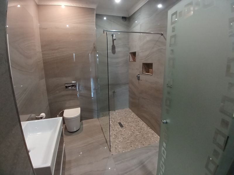 Modern bathroom featuring a walk-in shower with glass screen, recessed niches, wall-mounted toilet, and contemporary large-format tiling throughout.