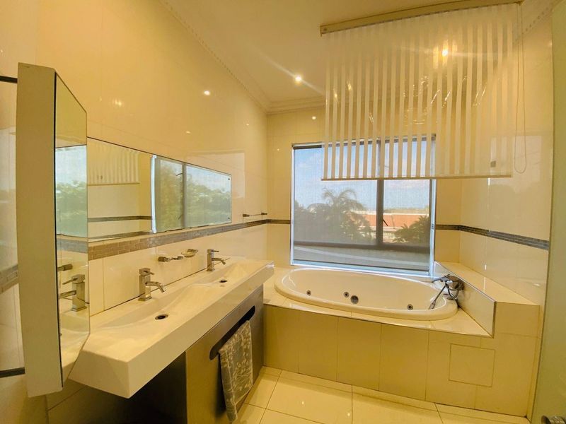 A well-maintained bathroom featuring a double vanity, a built-in bathtub, tiled finishes, and large windows providing natural light.