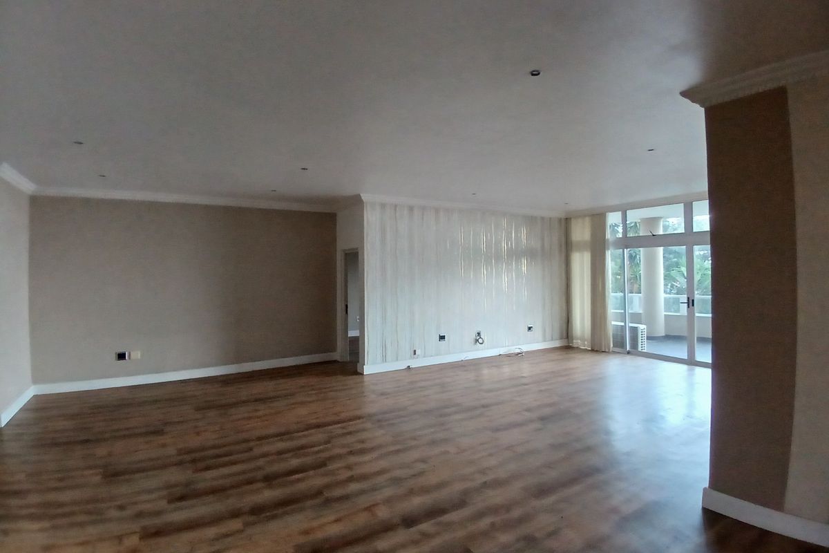 Spacious, empty living area featuring modern laminate flooring, recessed downlights, and large sliding glass doors leading to an outdoor balcony.
