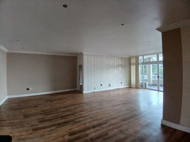 Spacious, empty living area featuring modern laminate flooring, recessed downlights, and large sliding glass doors leading to an outdoor balcony.