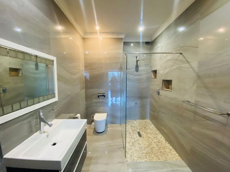Modern bathroom featuring a spacious walk-in shower with glass screen, wall-mounted vanity, and elegant floor-to-ceiling neutral-toned tiling.