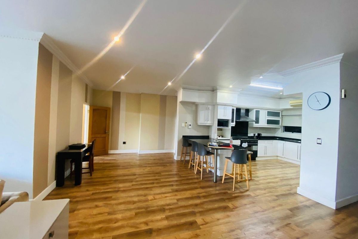 Spacious open-plan living area featuring modern kitchen cabinetry, granite countertops, breakfast bar, and warm laminate flooring throughout.